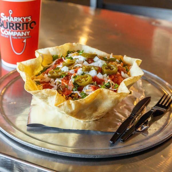 Sharky's Burrito Company taco salad in a fried tortilla bowl with a drink on a metal table.