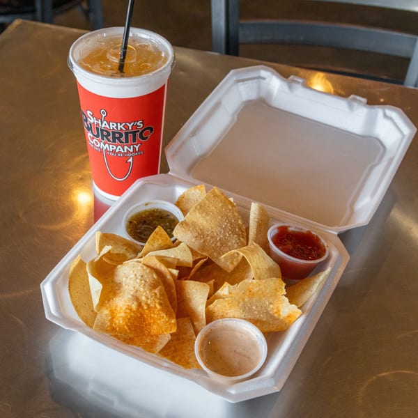 Sharky's Burrito Company chips and salsa with a drink on a metal table.