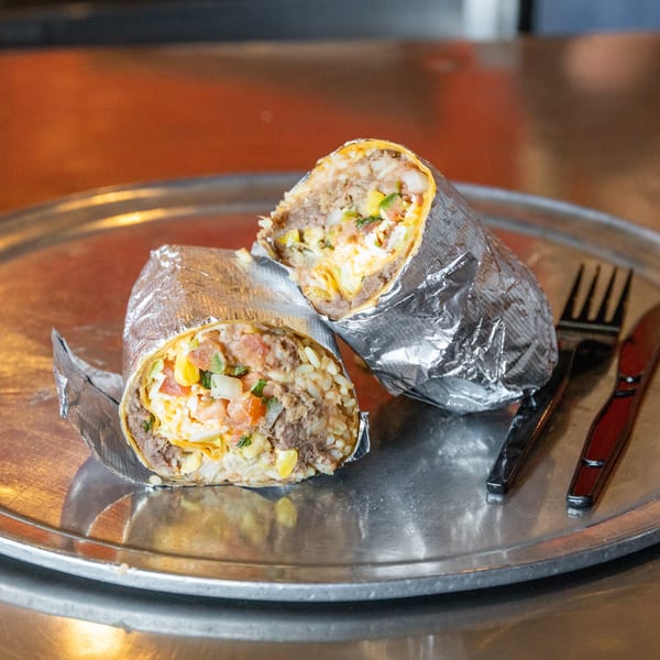 Two foil-wrapped burritos, cut in half to show fillings, on a metal plate with a fork and knife.